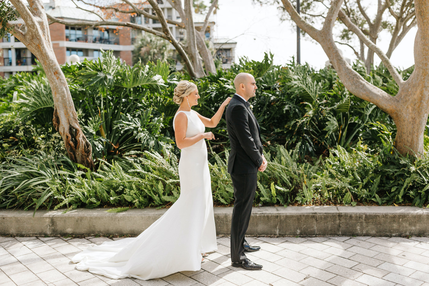 Bride and Groom Outdoor First Look | Simple Sheath Ivory Crepe Bateau Neck Low Back Bridal Gown by Theia | Groom in Classic Black Tux Suit with Bow Tie