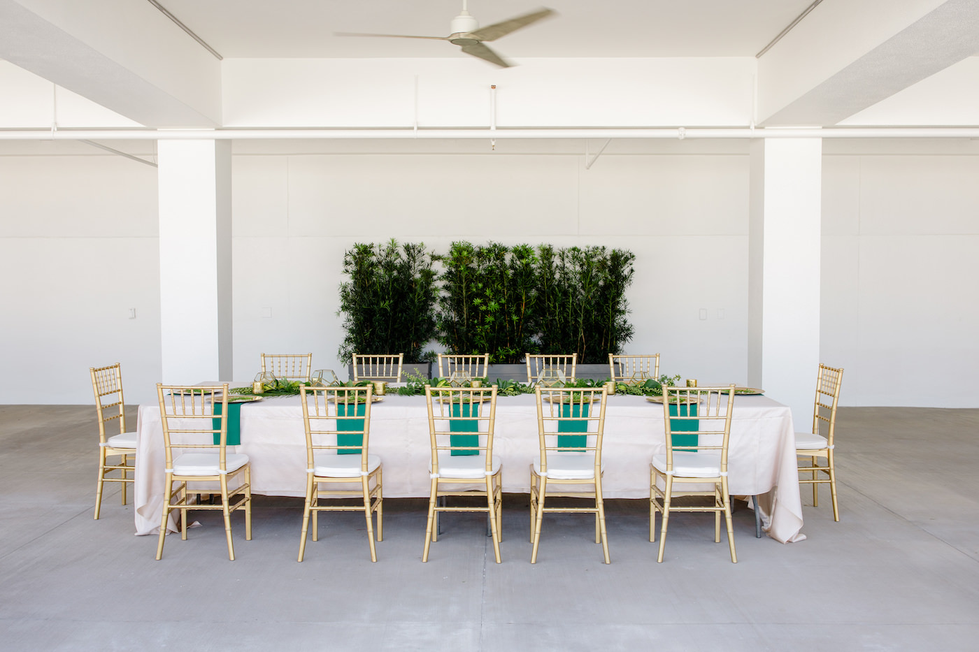 Clearwater Beach Wedding Venue Hilton Clearwater Beach | Modern Tropical Beach Outdoor Wedding Reception Terrace Feasting Table with Champagne Table Linens and Emerald Green Napkins under Gold Charger Plates | Gold Chiavari Chairs and Tropical Palm Frond Leaf Floral Arrangement Garland