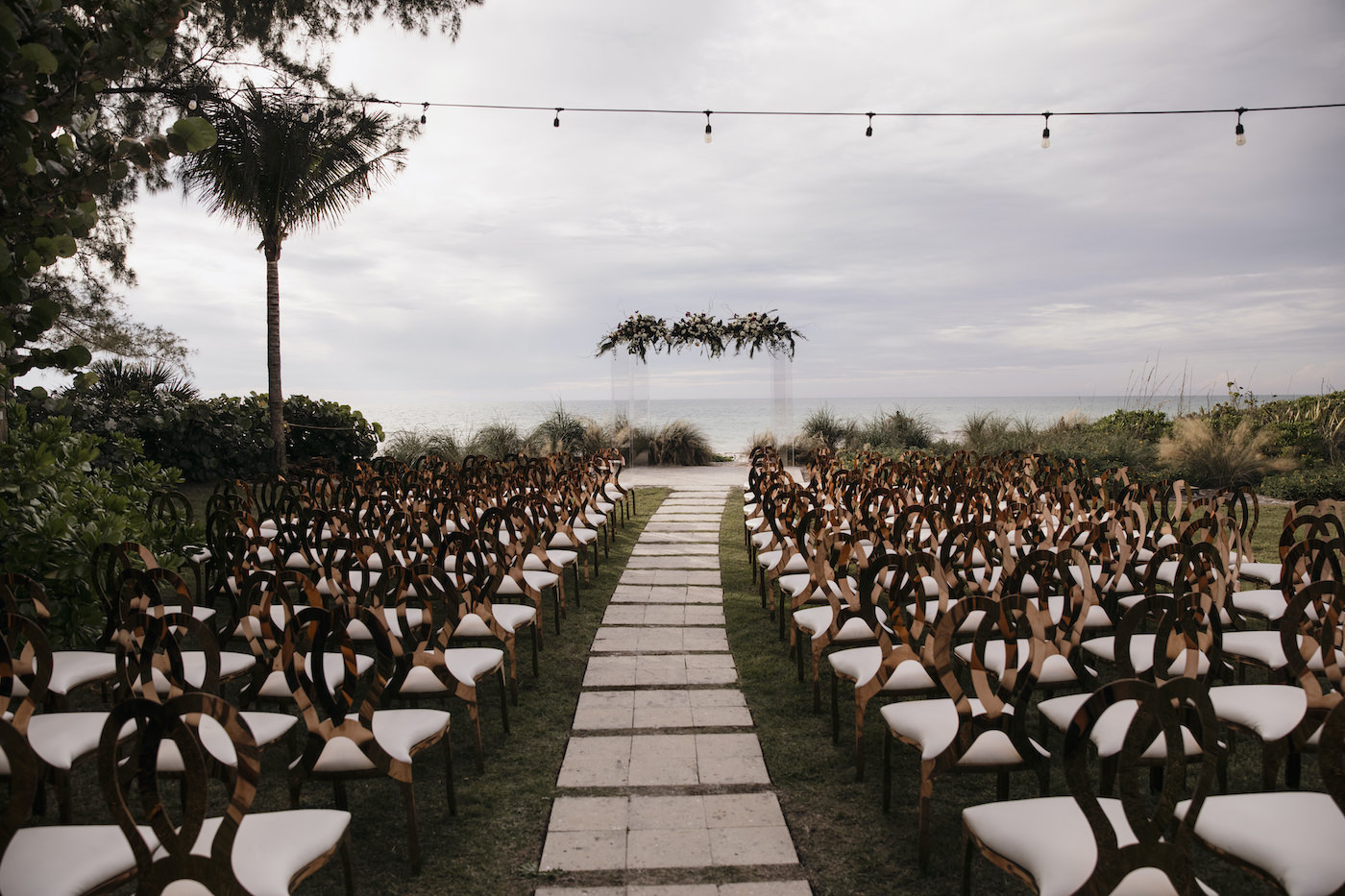 Sarasota Outdoor Beach Wedding Ceremony on Siesta Key | Acrylic Four Post Arbor Backdrop with White and Deep Red and Blush Pink Floral Arrangement Garland with Eucalyptus Greenery | Gold King Louis Chairs