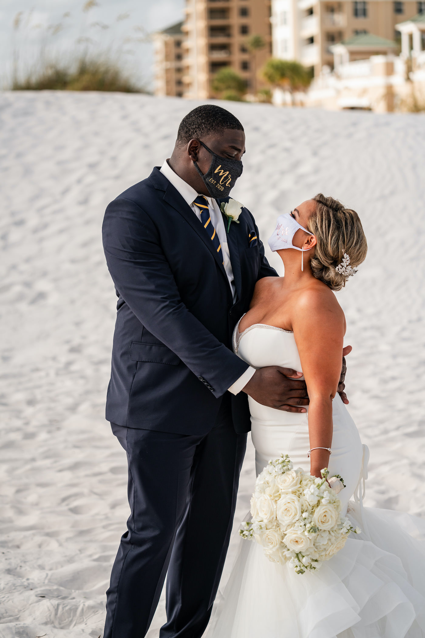 Destination Wedding During Pandemic. COVID Bride and Groom Beachfront Wedding Portraits Wearing Mr. and Mrs. Masks, Romantic Tropical Bride and Groom Just Married on the sand of Clearwater Beach, Bride Wearing Sophisticated Fit and Flare Strapless Wedding Dress | Florida Gulf of Mexico Hotel and Wedding Venue Hilton Clearwater Beach