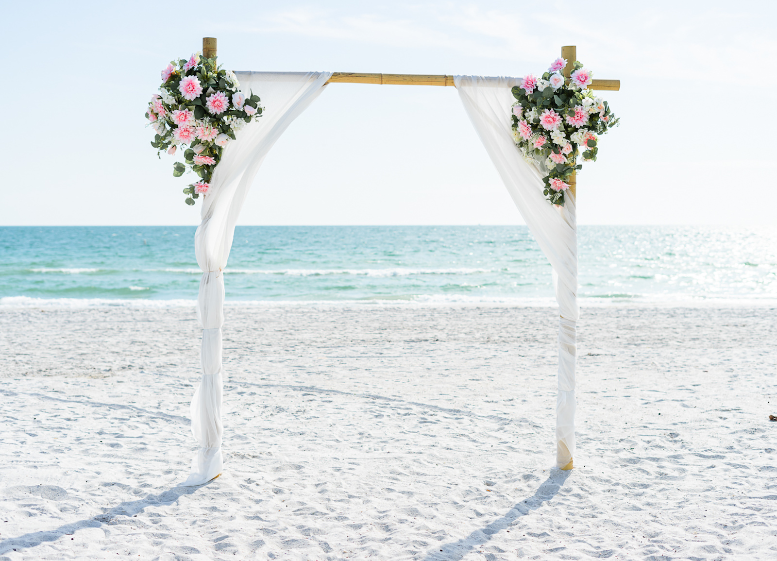 St. Petersburg Florida Beach Wedding Ceremony | Bamboo Arch Backdrop with Sheer White Draping and Blush Pink Floral Arrangements