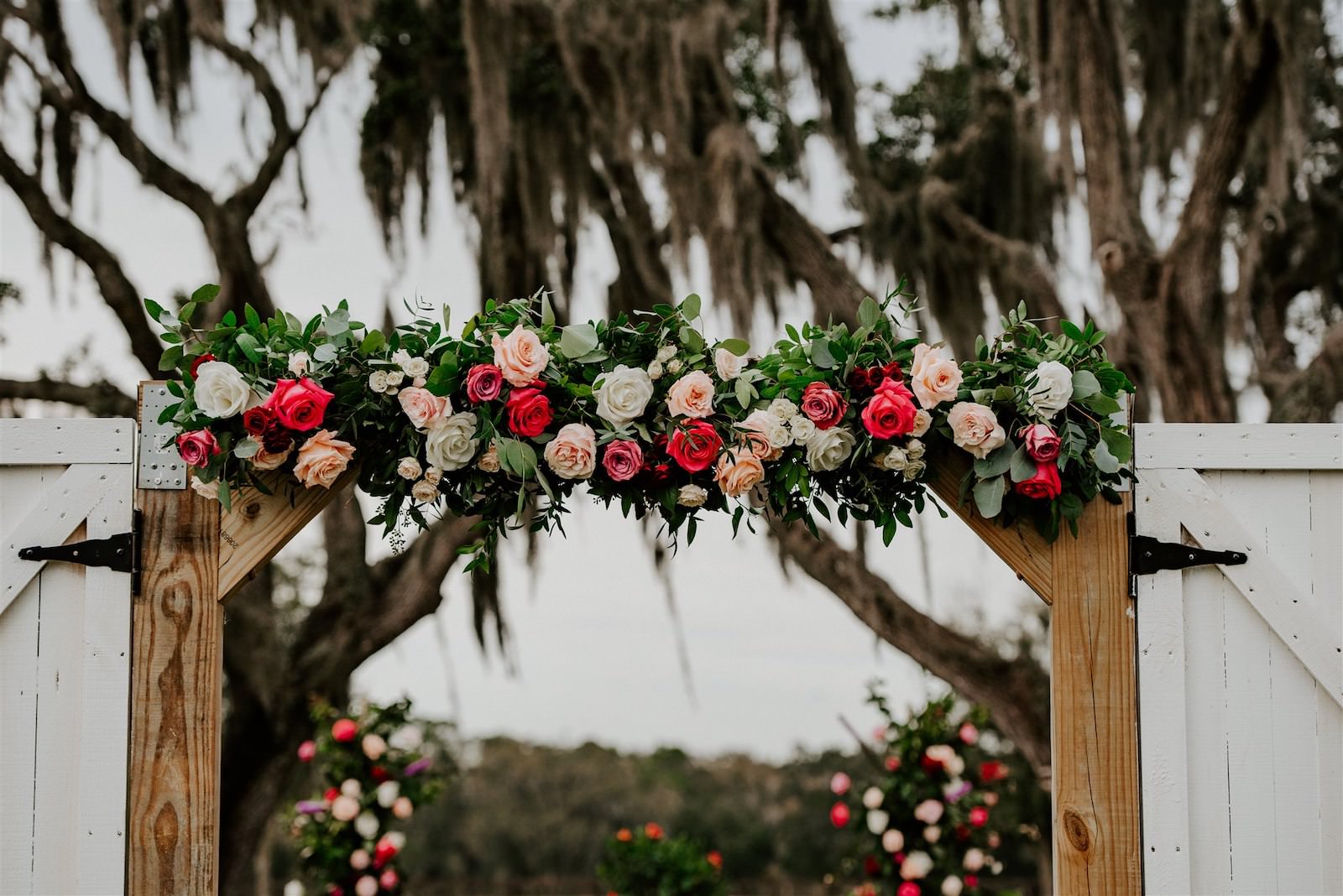 Wedding Barn Doors Entrance with Floral Garland | Tampa Wedding Florist Monarch Events and Designs | Deep Red Maroon Burgundy Roses and Blush Pink and White Roses with Eucalyptus Greenery