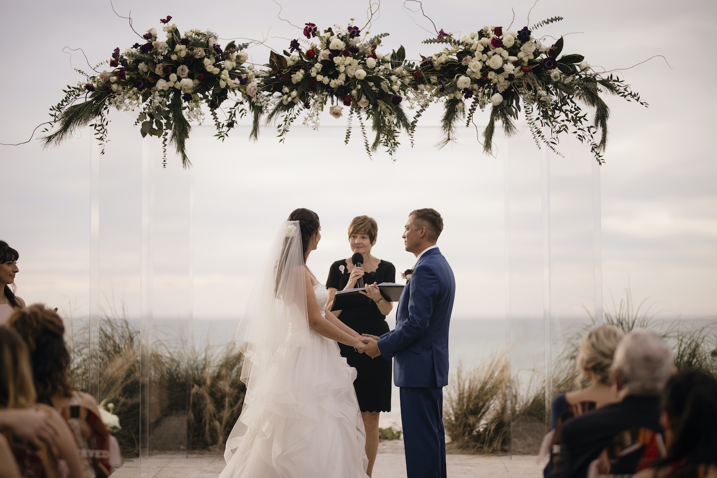 Bride and Groom Exchanging Vows at Sarasota Outdoor Beach Wedding Ceremony on Siesta Key | Acrylic Four Post Arbor Backdrop with White and Deep Red and Blush Pink Floral Arrangement Garland with Eucalyptus Greenery | Tampa Florida Wedding Officiant A Wedding With Grace