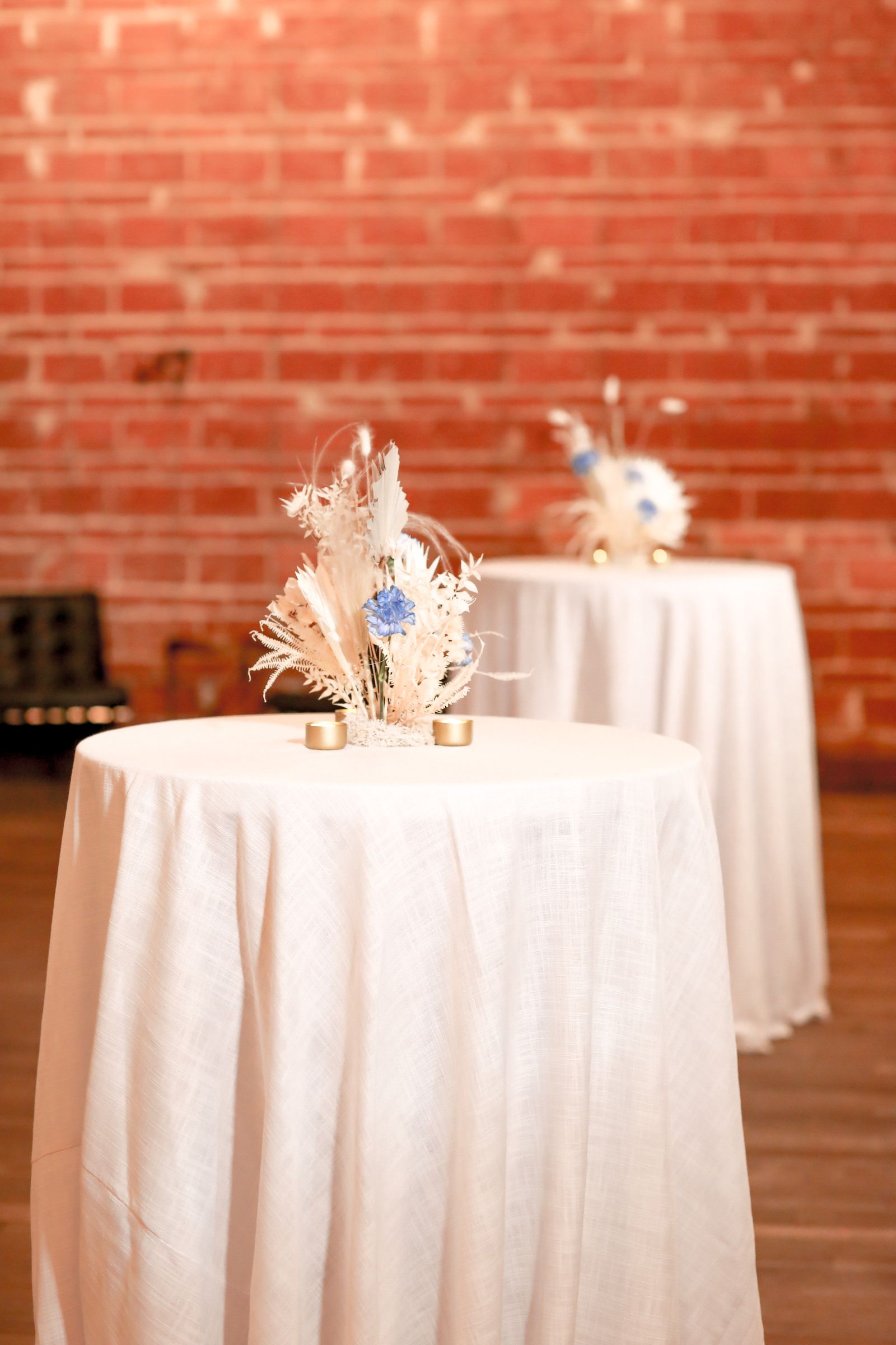 Tall Cocktail Tables with White Table Linens, Whimsical Wedding Reception Floral Centerpiece Decor, White Feathers and Blue Flowers, Red Brick Wall Backdrop | NOVA 535 | Over the Top Rental Linens | John Campbell Weddings
