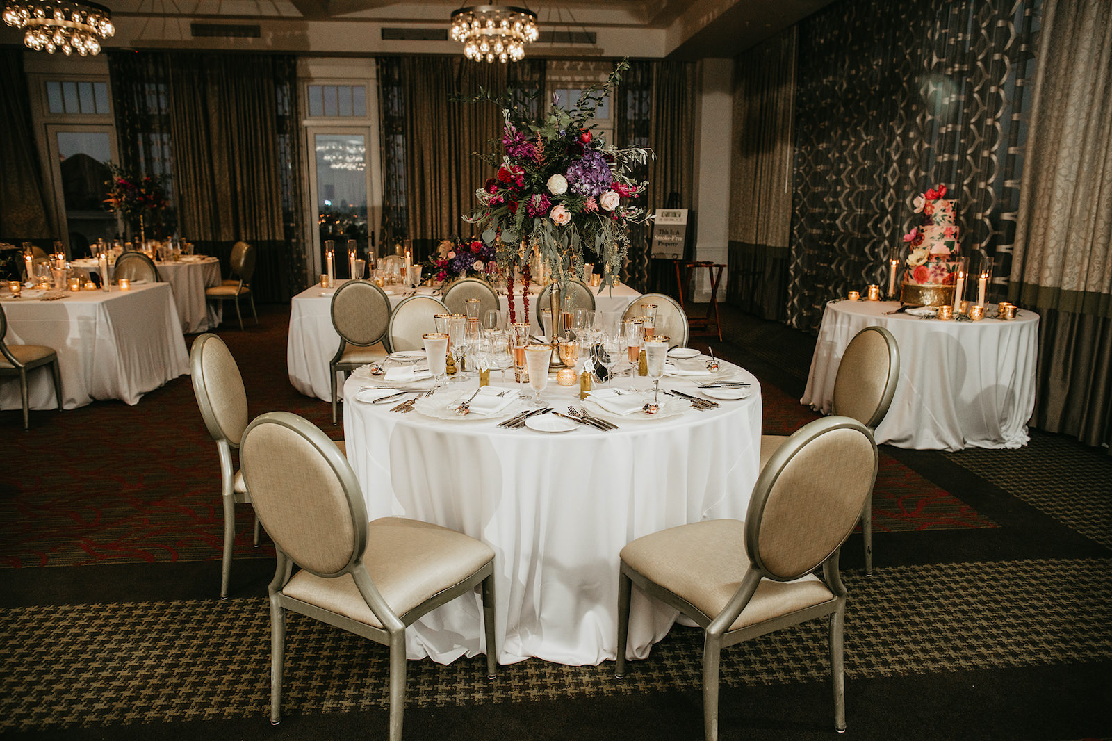 St. Pete Wedding Venue The Birchwood | Indoor Ballroom Wedding Reception with White Linen Tablecloth and Tall Floral Candlestick Centerpieces with Deep Purple and Burgundy Floral Arrangement