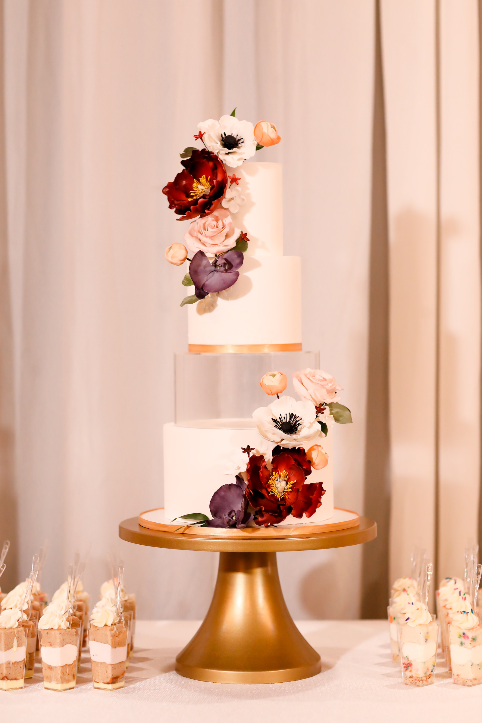 Modern Classic Four Tiered Round White and Gold Wedding Cake with Acrylic Tier and Purple, Red and Blush Pink Sugar Flowers | Individual Confetti Cake Cups | Tampa Bay Cake Company