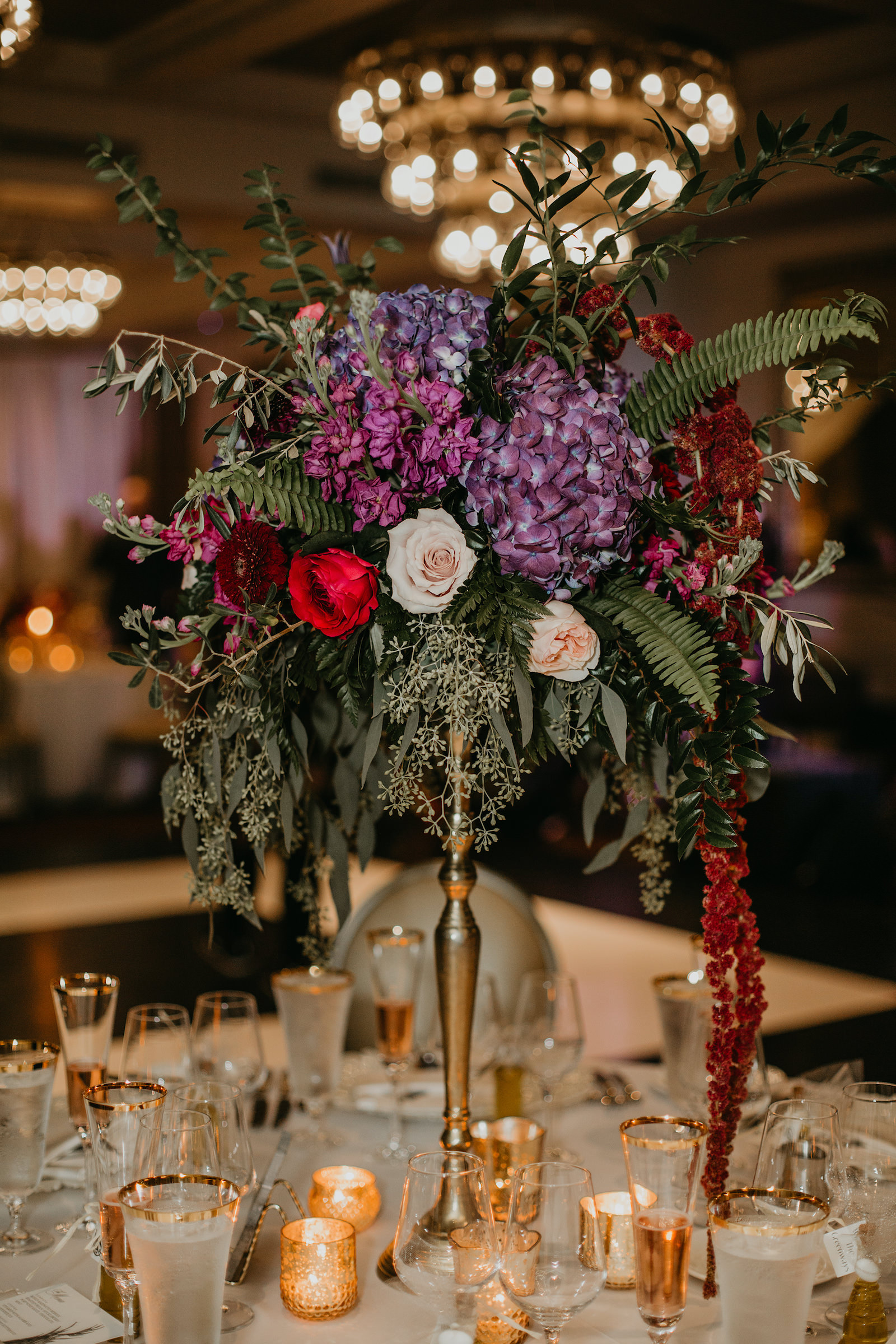 Wedding Centerpiece Inspiration | Tall Candlestick Centerpiece with Loose Cascading Floral Arrangement of Purple Hydrangea, Deep Red Burgundy Roses and Amaranthus, Olive Branches and Eucalyptus Greenery