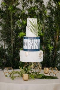 Clearwater Beach Wedding Venue Hilton Clearwater Beach | Modern Tropical Beach Outdoor Wedding Cake Table with Four Tier Gold and Navy Wedding Cake accented with Palm Frond Leaf on Gold Geometric Stand | The Artistic Whisk