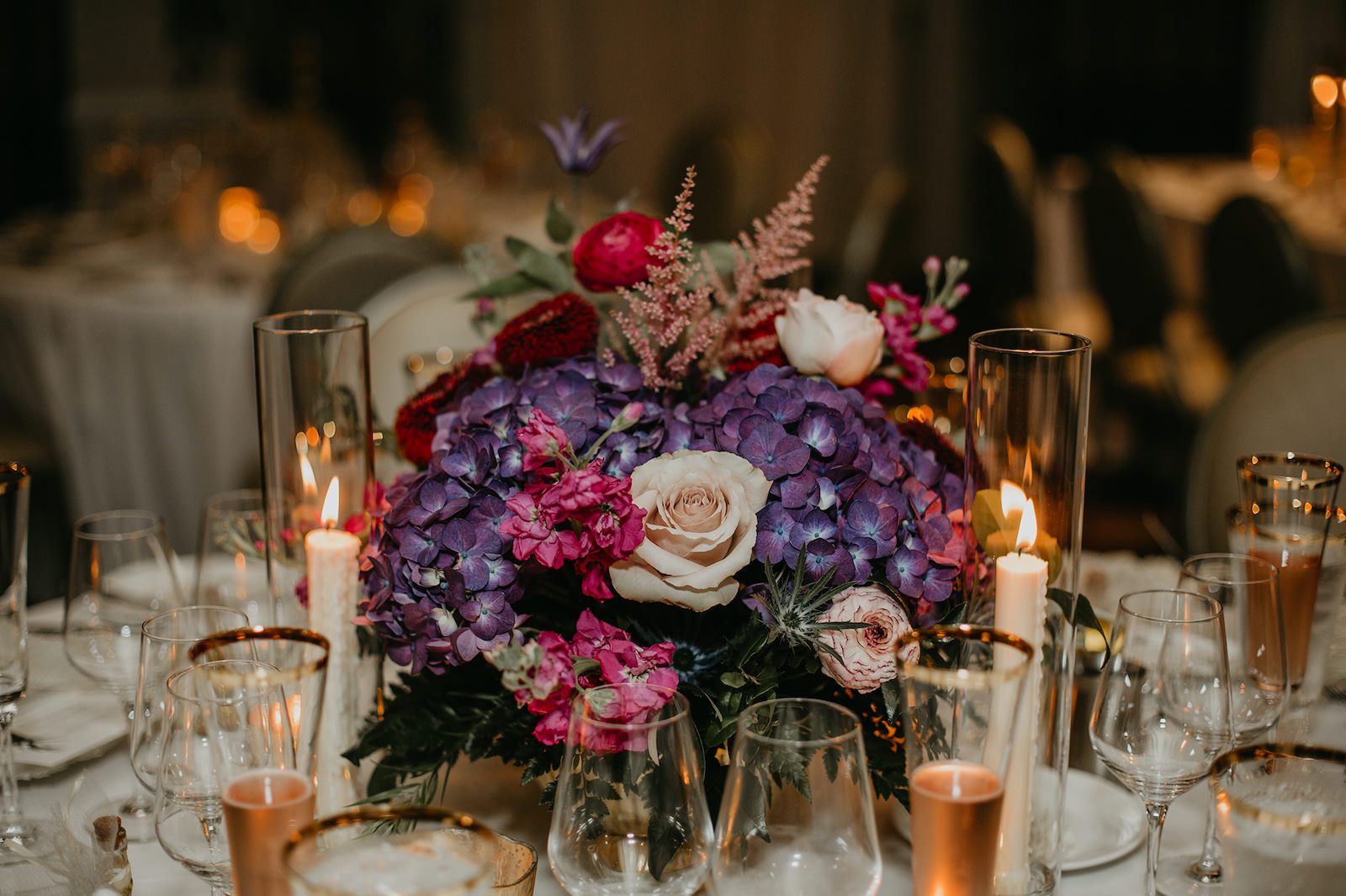 Wedding Centerpiece Inspiration | Low Compote Centerpiece with Floral Arrangement of Purple Hydrangea, Blush Pink Astilbe and Stock, Deep Red Burgundy Ranunculus and Greenery with Taper Candles