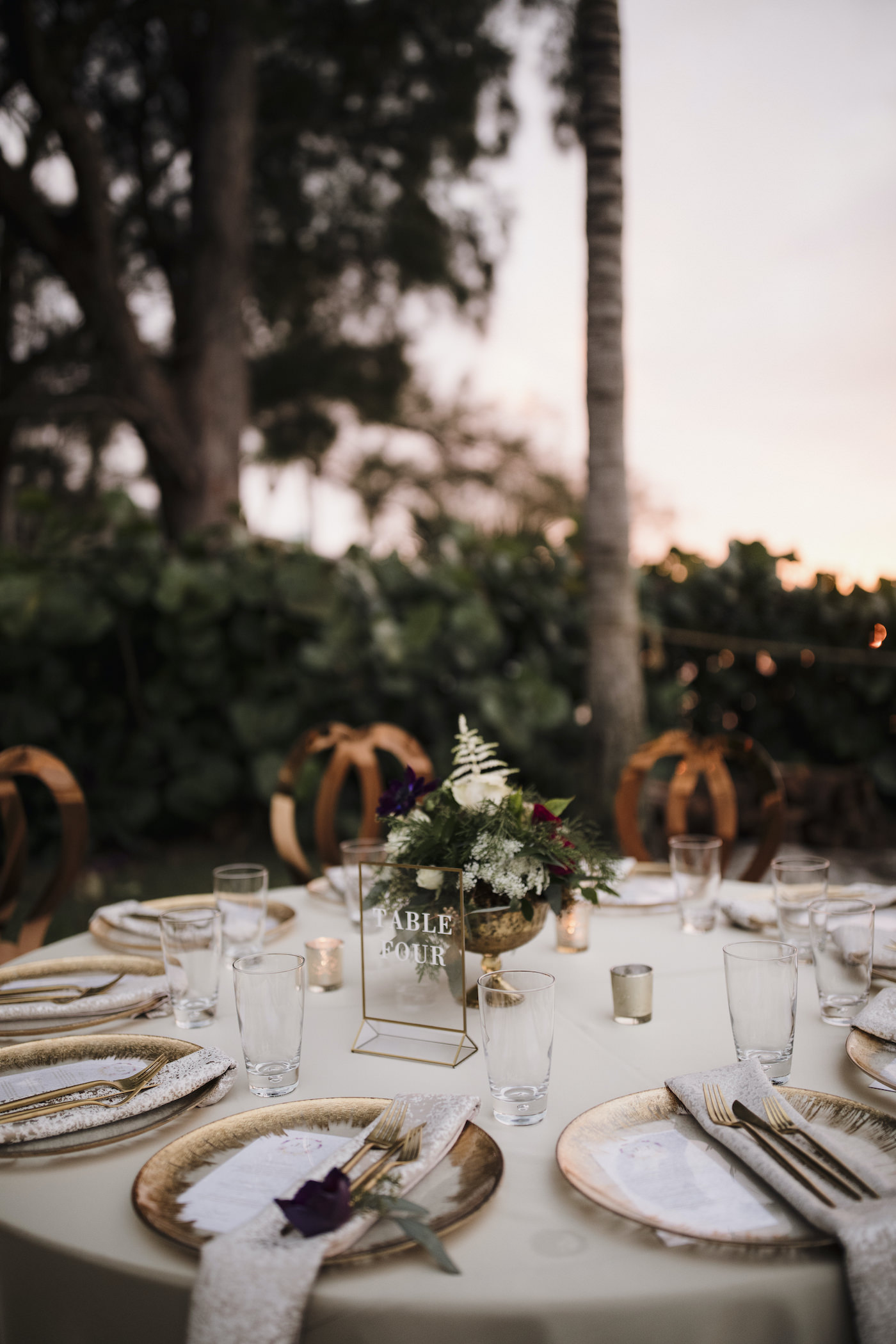 Outdoor Sarasota Beach Neutral Gold and Champagne Wedding Reception Table with Gold Glass Charger Plates and Gold Flatware and Gold King Louis Chairs | Gold Geometric Glass Frame Table Number | Gold Compote Vase Wedding Centerpiece with White and Red Flowers and Greenery