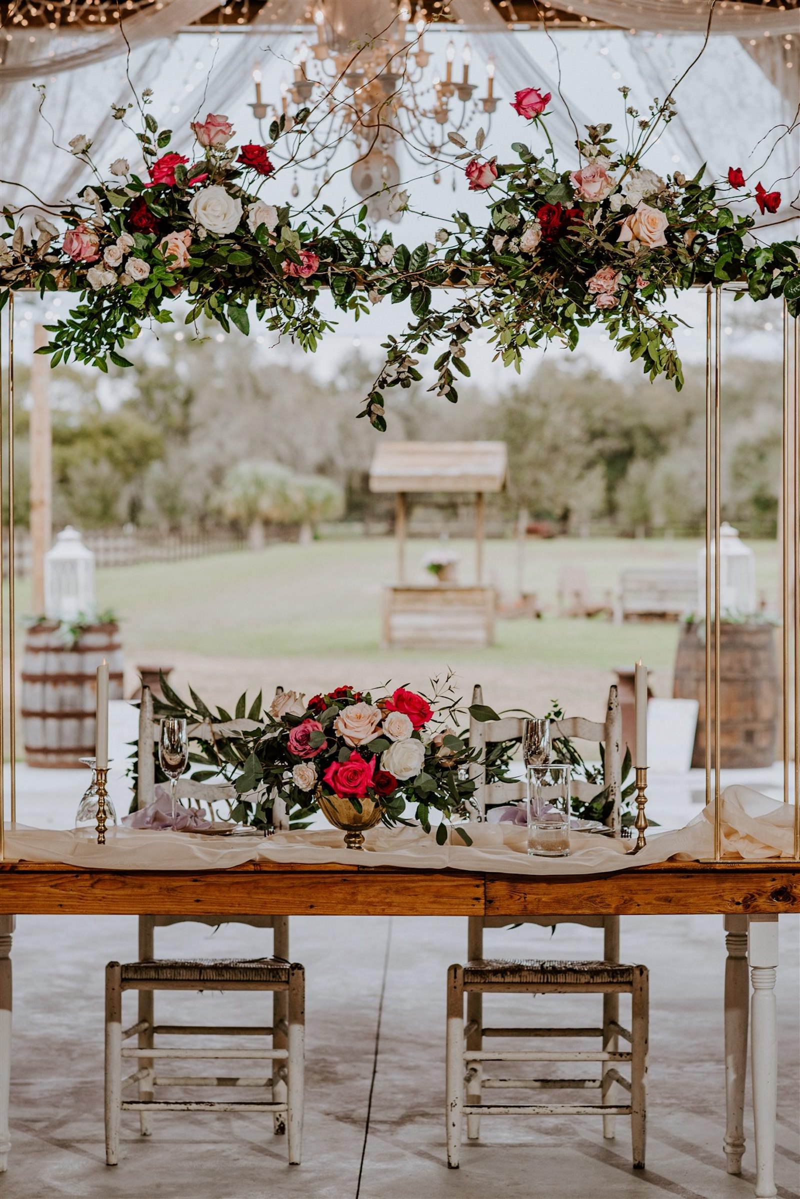Rustic Barn Tampa Wedding with Suspended Ceiling Floral Arrangements with Blush Pink and Deep Red Burgundy Roses and Greenery | Wood Farm Sweetheart Table with Champagne Linen Runners and Taper Candlestick Candles | Tampa Wedding Florist Monarch Events and Designs