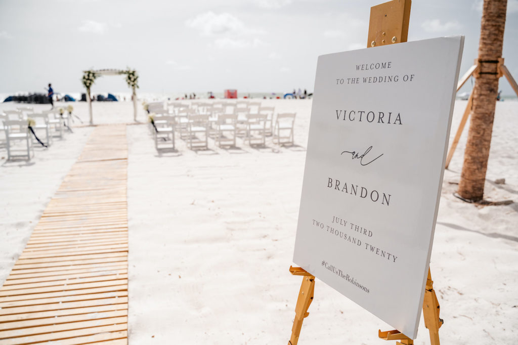 Tampa Bay Beach Wedding Ceremony, Outdoor Beachfront Ceremony on the White Powder Sand with Tropical Decor, Elegant Black Script Welcome Sign Victoria and Brandon, Bamboo Wooden Aisle Runner | Florida Hotel and Wedding Venue Hilton Clearwater Beach