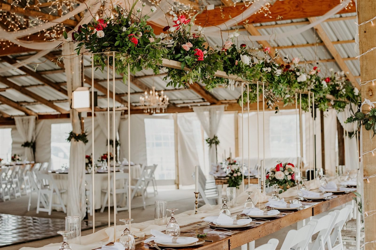 Rustic Barn Tampa Wedding with Suspended Ceiling Floral Arrangements with Blush Pink and Deep Red Burgundy Roses and Greenery | Wood Farm Tables with Champagne Linen Runners and Taper Candlestick Candles | Tampa Wedding Florist Monarch Events and Designs
