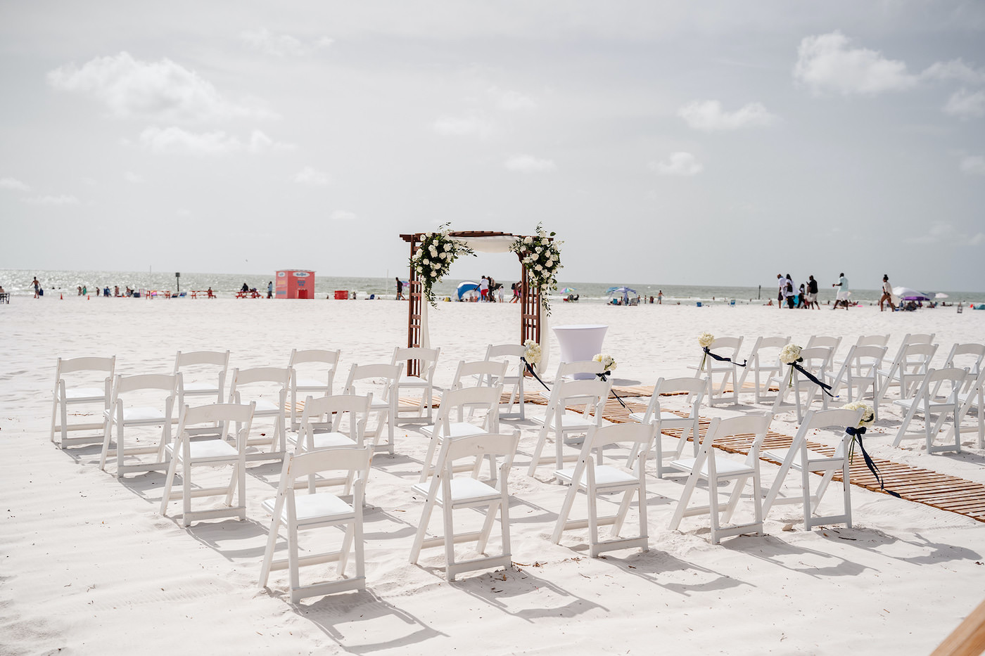 Tampa Bay Beach Wedding Ceremony, Outdoor Beachfront Ceremony on the White Powder Sand with Tropical Decor, Wooden Arch with Elegant White Floral Bouquets with Greenery, Bamboo Wooden Aisle Runner | Florida Hotel and Wedding Venue Hilton Clearwater Beach