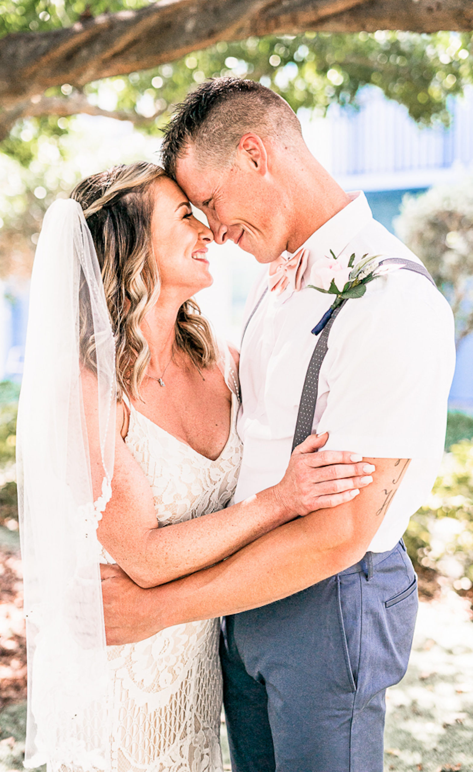 St. Petersburg Florida Wedding | Outdoor Bride and Groom Portrait at Wedding Venue Postcard Inn on the Beach | Groom Navy Blue Pants with White Short Sleeve Shirt and Suspenders and Flip Flops | Lace Sheath Spaghetti Strap V Neck Boho Bridal Gown Wedding Dress