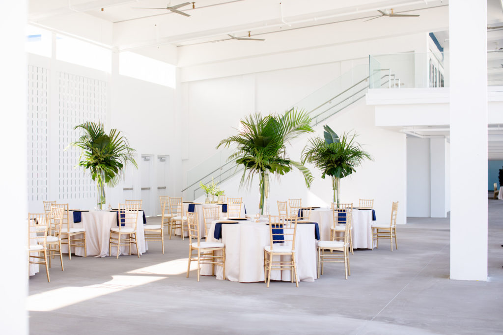 Clearwater Beach Wedding Venue Hilton Clearwater Beach | Modern Tropical Beach Outdoor Wedding Reception Terrace with White Table Linens and Gold Chiavari Chairs and Champagne Sash Bows and Tropical Palm Frond Leaf Floral Arrangement Centerpieces
