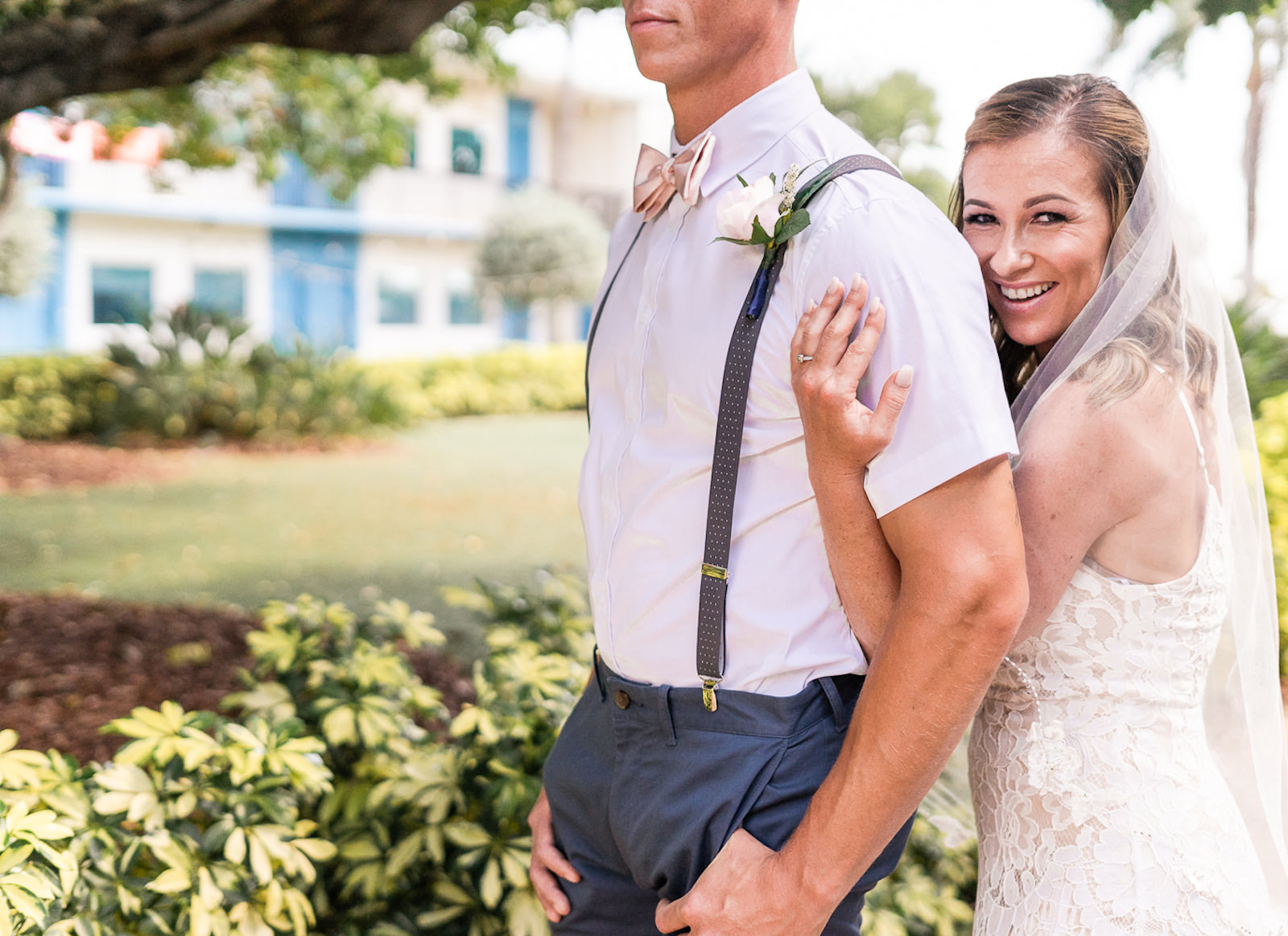 St. Petersburg Florida Wedding | Outdoor Bride and Groom Portrait at Wedding Venue Postcard Inn on the Beach | Groom Navy Blue Pants with White Short Sleeve Shirt and Suspenders and Flip Flops | Lace Sheath Spaghetti Strap V Neck Boho Bridal Gown Wedding Dress