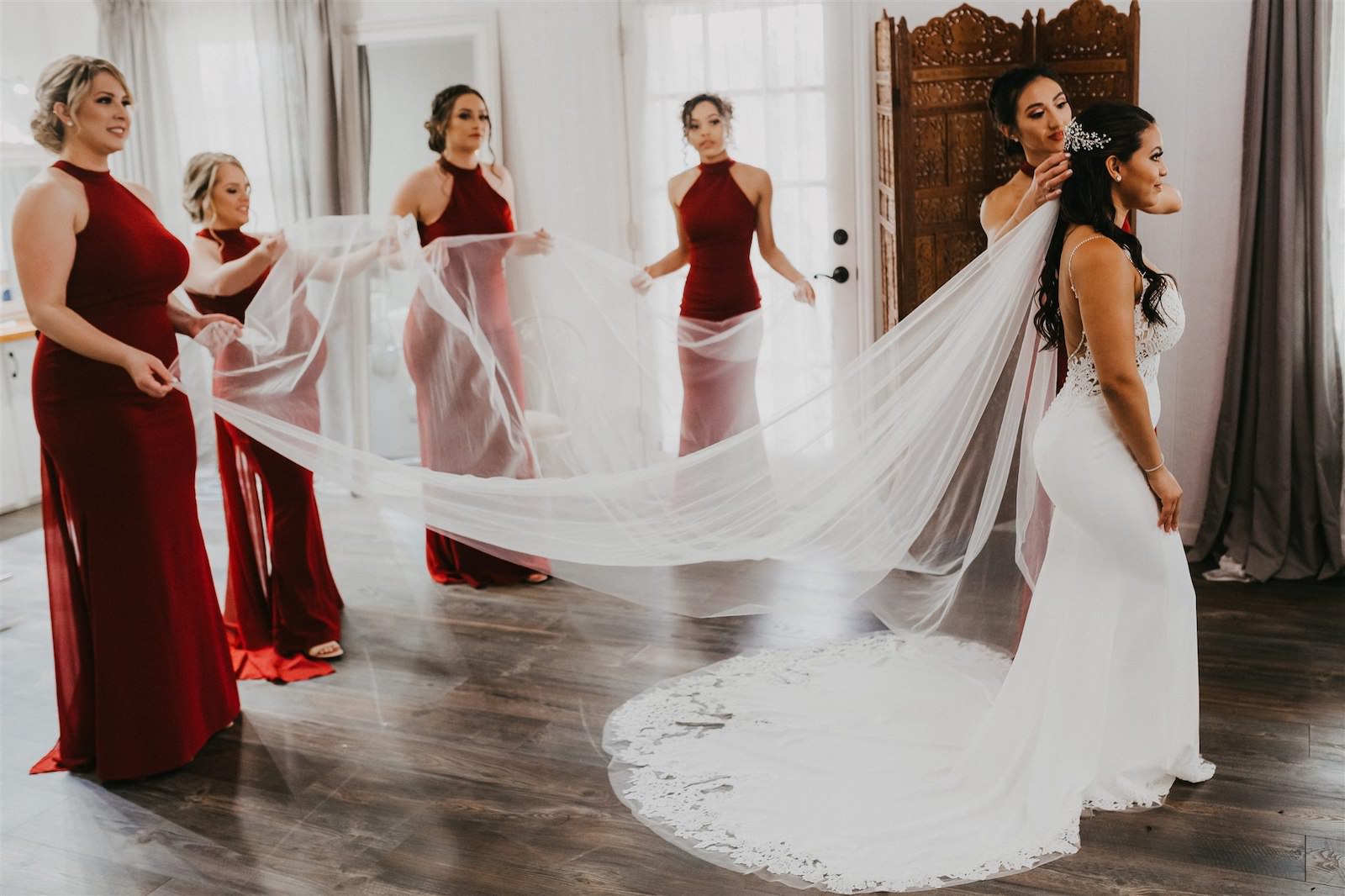 Bridesmaids Helping Bride Get Ready Shot | Femme Akoi Beauty Studio Wedding Hair and Makeup | Enzoani Lace Mermaid Low Back Spaghetti Strap Dress with Cathedral Veil | Burgundy Maroon Deep Red Chiffon Bridesmaid Dresses
