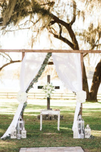 Rustic Elegant Wedding Ceremony and Decor, Wooden Arch, Crucifix Cross Backdropm White Draping with Eucalyptus Leaf Greenery, Vintage Ivory Bird Cages, Antique End Table for Pulpit | Tampa Bay Luxury Wedding Planner and Floral Designer John Campbell Weddings | Covington Farm