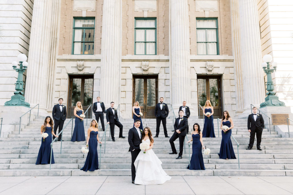 Bride, Groom and Wedding Party Portrait on Steps of Historic Boutique Downtown Tampa Hotel Le Meridien, Bridesmaids in Matching Navy Blue Dresses, Groomsmen in Black Tuxedos | Tampa Dress Shop Bella Bridesmaids | Special Moments Event Planning