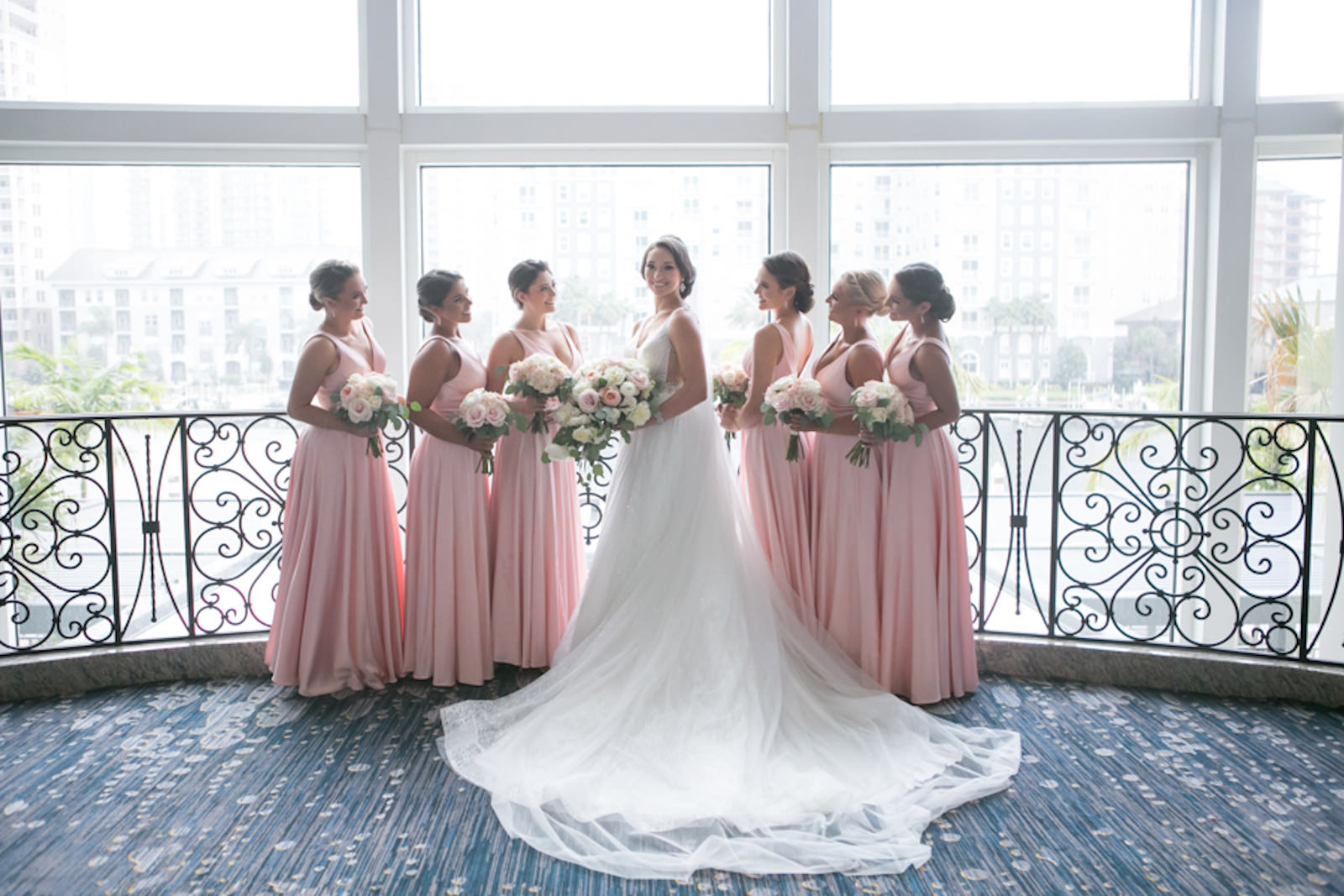 Indoor Downtown Tampa Hotel Window Bridall Party Portrait with Bride and Bridesmaids | V Neck Illusion Lace A Line Ballgown Wedding Dress with Rhinestone Waist Band and Cathedral Veil | Blush Pink and White Roses and Peonies Wedding Bridal Bouquets | Blush Pink Long Silk Satin Formal Bridesmaid Dresses