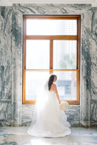 Elegant Bride in Ballgown Hayley Paige Wedding Dress and Veil Holding Classic Floral Bouquet in front of Window and Marble Gray Wall at Historic Boutique Hotel in Downtown Tampa Le Meridien