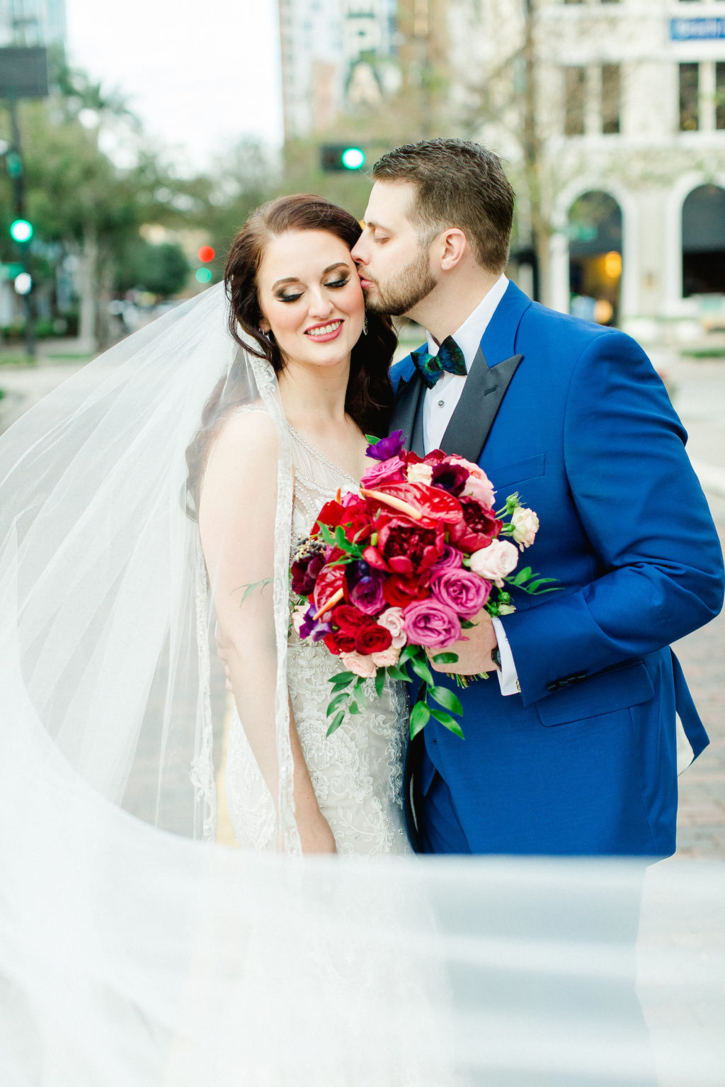 Bride and Groom Outdoor Downtown Tampa Wedding Portrait Veil Shot | Groom in Blue Suit with Black Satin Lapel | Rhinestone Embroidered Wedding Dress Bridal Gown | Bright Colorful Red and Pink Wedding Bridal Bouquet
