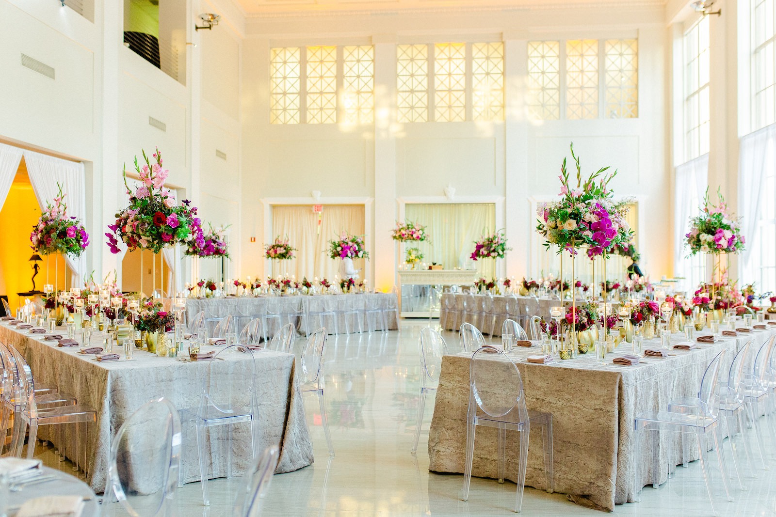 Colorful Luxury Indoor Wedding Reception at Tampa Wedding Venue The Vault | Feasting Tables with Ghost Chairs and Tall Centerpieces of Pink Gladiolas, Roses, Orchids and Greenery with Gold Bud Vases and Candles | Kate Ryan Event Rentals