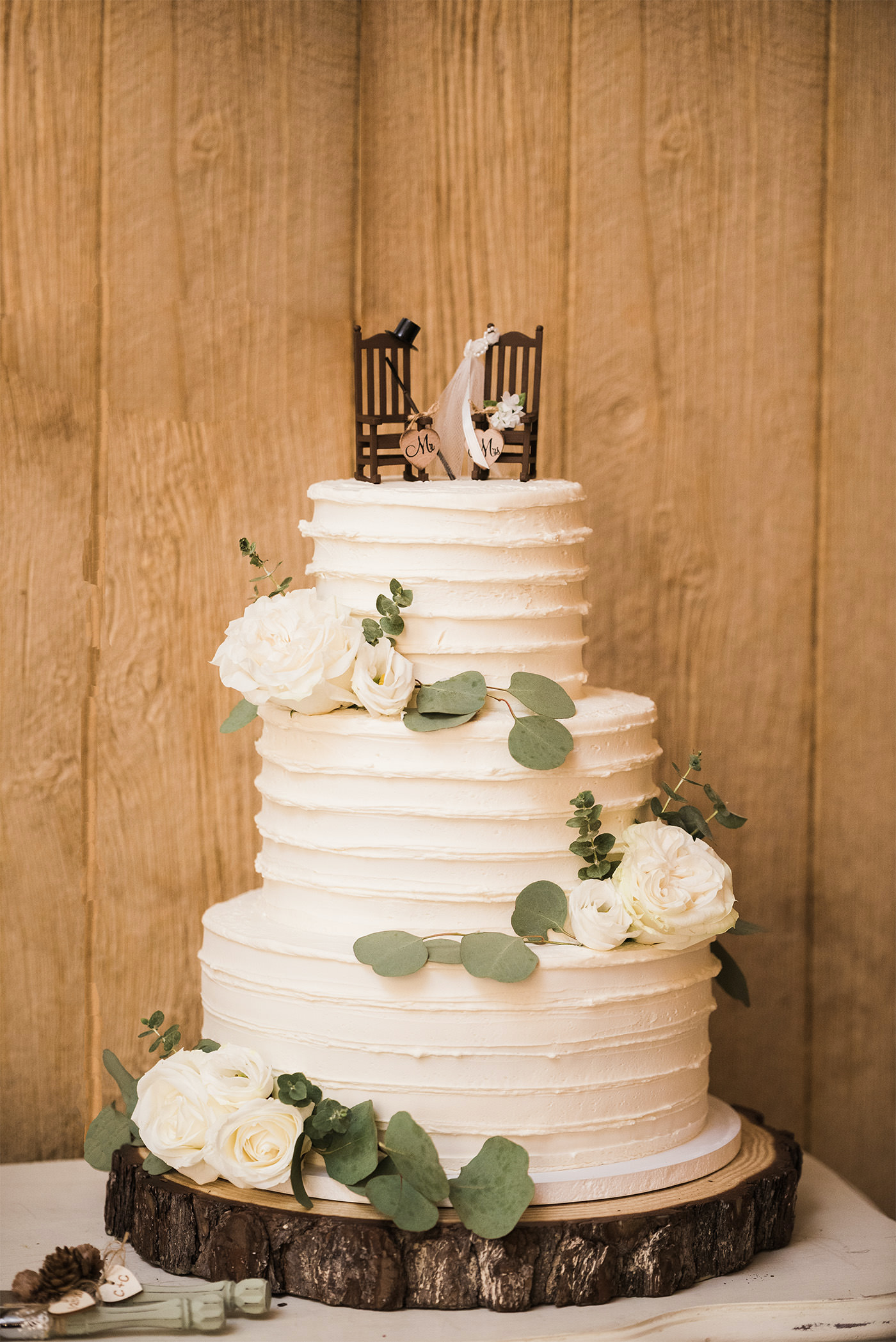 Rustic Chic Three Tier Wedding Cake with White Buttercream Frosting, Horizontal White Stripes, Rose Floral Accents, His and Her Rocking Chair Cake Topper, Wooden Tree Truck Cake Stand