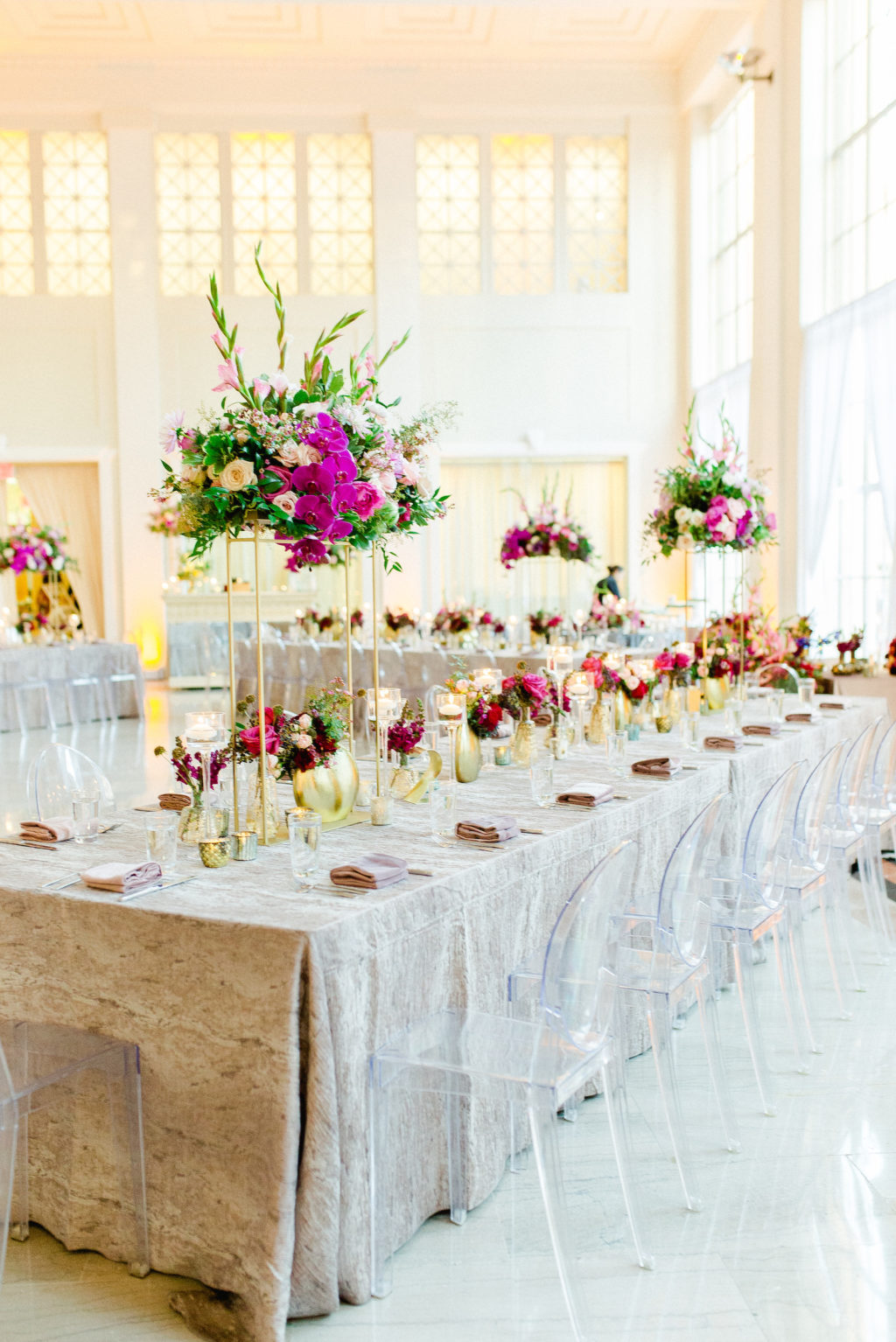 Colorful Luxury Indoor Wedding Reception at Tampa Wedding Venue The Vault | Feasting Tables with Ghost Chairs and Tall Centerpieces of Pink Gladiolas, Roses, Orchids and Greenery with Gold Bud Vases and Candles | Kate Ryan Event Rentals