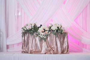 Tampa Blush Pink and Gold Wedding Sweetheart Table with Rose Gold Sequin Table Linen and Ivory and Blush Floral Arrangement Centerpieces with Roses, Hydrangea, and Eucalyptus Greenery | Pipe and Drape Backdrop with Pink Uplighting by Gabro Event Services