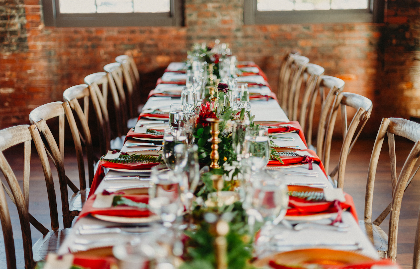Tampa Wedding Reception at Historic Building Armature Works with Brick Walls | Long Feasting Tables with Wood Cross Back Chairs and Greenery Garland Runners with Gold Candlesticks and Burgundy Maroon Red Napkins