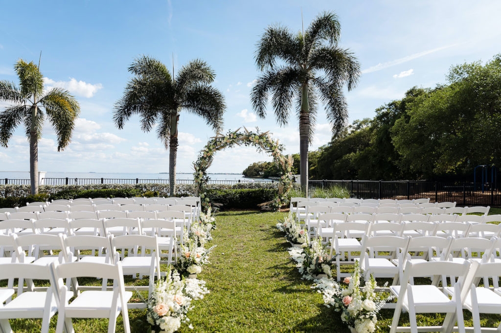 Whimsical Waterfront Wedding Ceremony Decor, Garden Setting, Circular Floral Arch with Pampas Grass, White and Blush Pink Flowers and Greenery, Aisle Lined with Lush Floral Arrangements | Tampa Bay Wedding Planner Breezin' Weddings | Wedding Venue Tampa Yacht and Country Club
