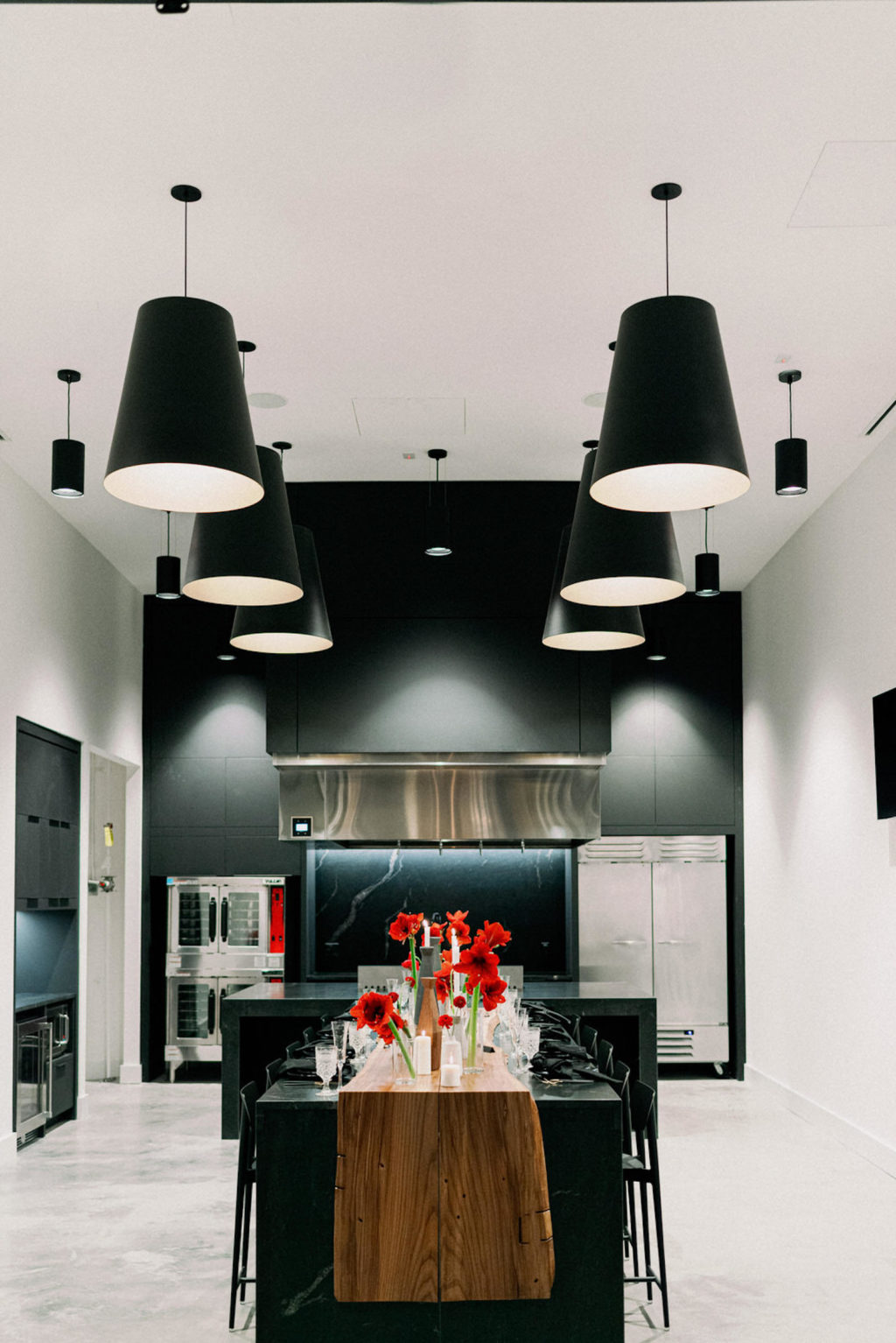 Modern Indoor South Tampa Wedding Space at Tampa Wedding Venue Hyde House | Test Kitchen Private Dinner Chef's Table Intimate Wedding | Long Black Feasting Table with Live Edge Wood and Red Amaryllis Bud Vase Centerpieces