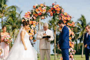 Bride and Groom Praying During Wedding Ceremony, Tropical Colorful Pink and Coral Floral and Palm Tree Leaves Lush Arch | Tampa Bay Wedding Planner NK Weddings