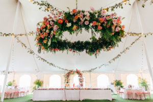 Tropical Elegant Tent Wedding Reception Decor, Lush Pink, Coral, Purple and Palm Tree Leaves Lush Floral Chandelier and Hanging Florals, Long Feasting Table with White Linens, Colorful Floral Arch Behind Sweetheart Table | Tampa Bay Wedding Planner NK Weddings