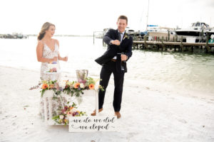 Florida Bride and Groom Pop Champagne after Intimate Florida Vow Exchange and Elopement Decor, Vibrant Florals with Yellow Sunflowers, White Florals, Orange, Pink and Purple Flowers, Small One Tier Top of Cake with Floral Embellishments | St. Petersburg Private Beachfront Wedding Venue Isla Del Sol | Florida Elopement Planner Elope Tampa Bay