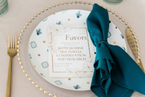 Tampa Florida Brunch Wedding Place Setting with Gold Glass Beaded Edge Chargers with Blue Pattern Fortessa Plates, Gold Flatware, Aqua Cups and Teal Turquoise Blue Napkins | Wedding Donation Favor Alternative Cards for Mote Marine Sea Turtles