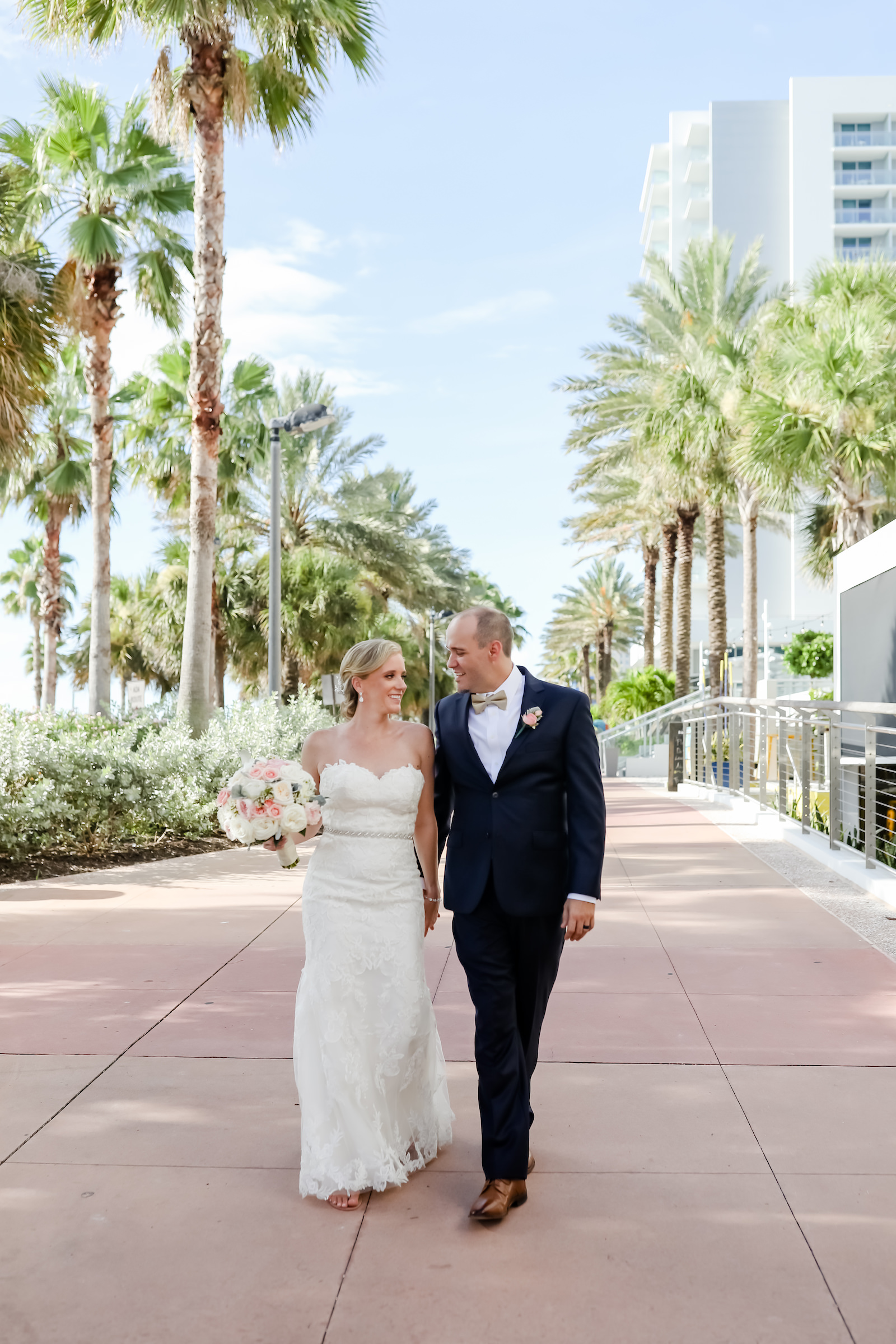 Bride and Groom Outdoor Portrait at Clearwater Beach Wedding | Bridal Gown Hanger Shot | Strapless Sweetheart Lace A Line Wedding Dress with Rhinestone Waistband | Blush Pink and White Rose Bouquet | Groom in Classic Navy Blue Suit with Champagne Bow Tie | Lifelong Photography Studios