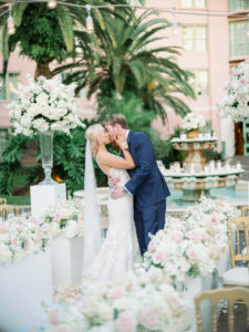 Romantic Florida Bride and Groom Kiss Intimate Embrace at Outdoor Garden Wedding Ceremony, Decorated with Elegant Tall Rose Floral Arrangements, Ivory, Blush Pink, and White Flowers Bride Wearing Eve of Milady Kleinfeld Bridal Dress, Groom in Navy Suit with Champagne Rose Boutonniere | Tampa Bay Wedding Planner Parties A'La Carte | Tea Garden Ceremony at Florida Wedding Venue and Historic Resort The Vinoy Renaissance in Downtown St. Petersburg