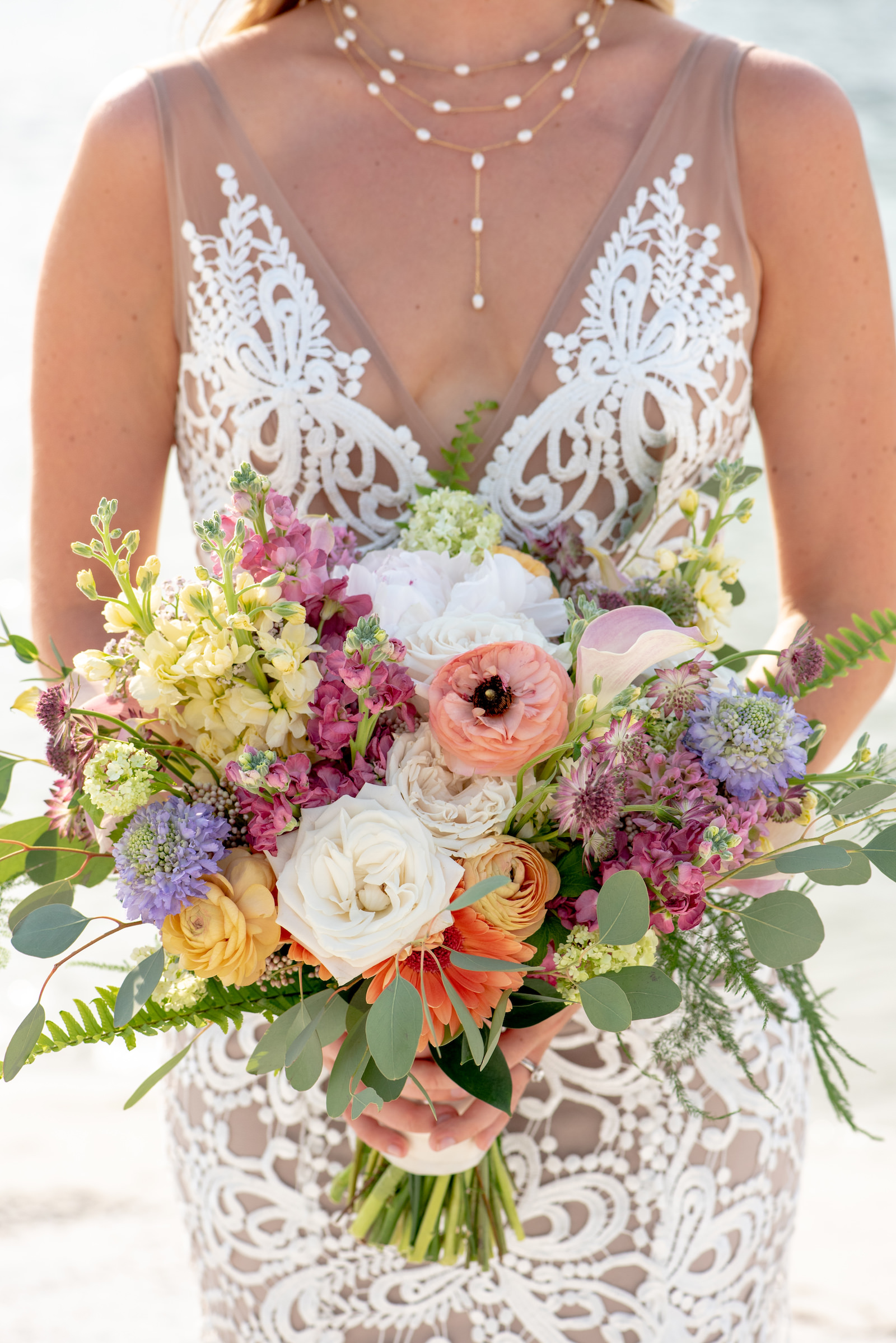 Tampa Bay Bride holding Springtime Vibrant Floral Bouquet, with Peach, Purple, Pink, Yellow, Purple and Orange Florals, Bride wearing Boho Chic Made with Love Bridal Wedding Dress