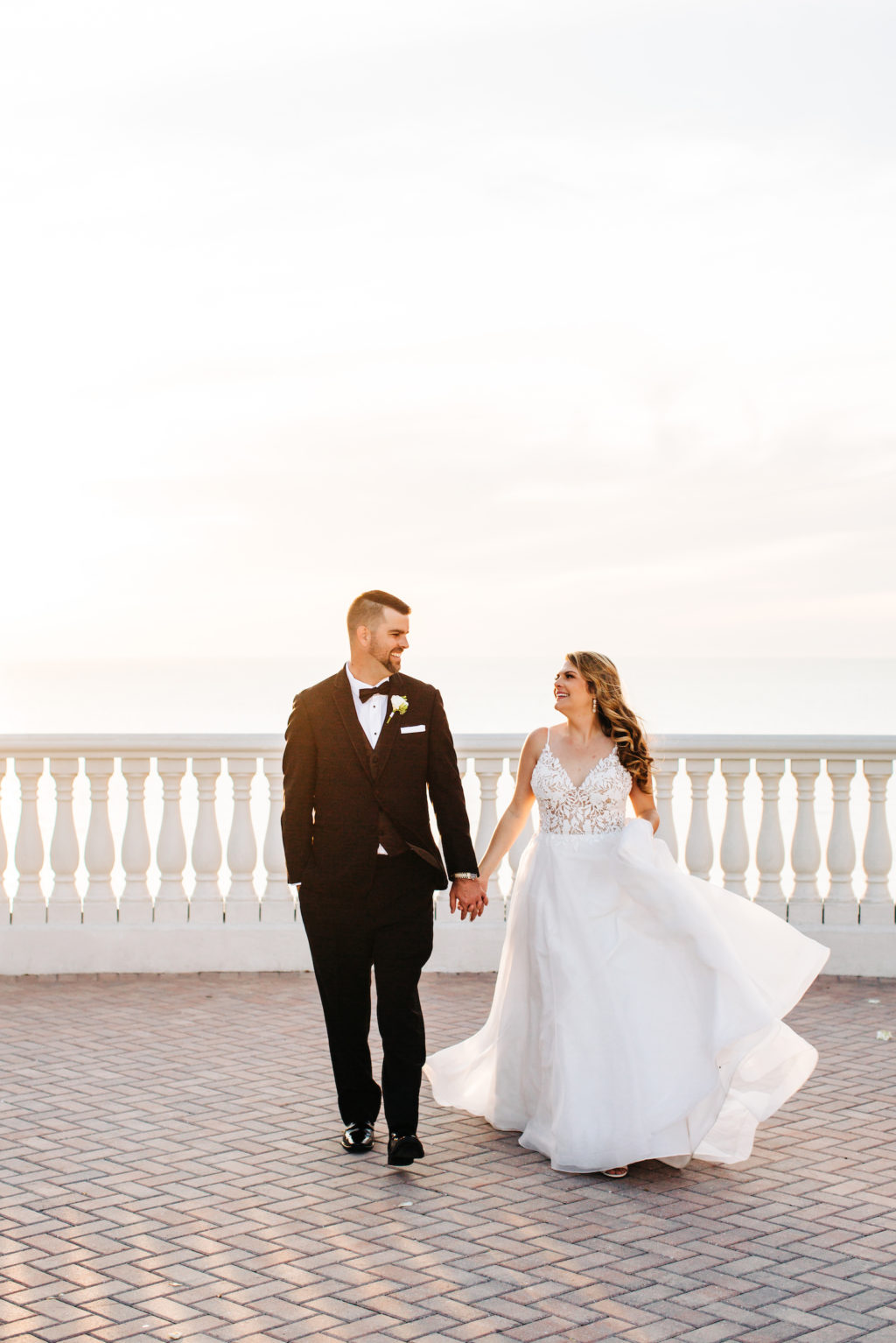 Tampa Bay Bride and Groom Wedding Portrait at Sunset on Waterfront Hotel Rooftop Balcony, Bride Wearing Romantic A Line Mikaella Bridal Wedding Dress, Groom in Classic Black Tuxedo with Bowtie | Florida Wedding Venue and Resort Hyatt Regency Clearwater Beach