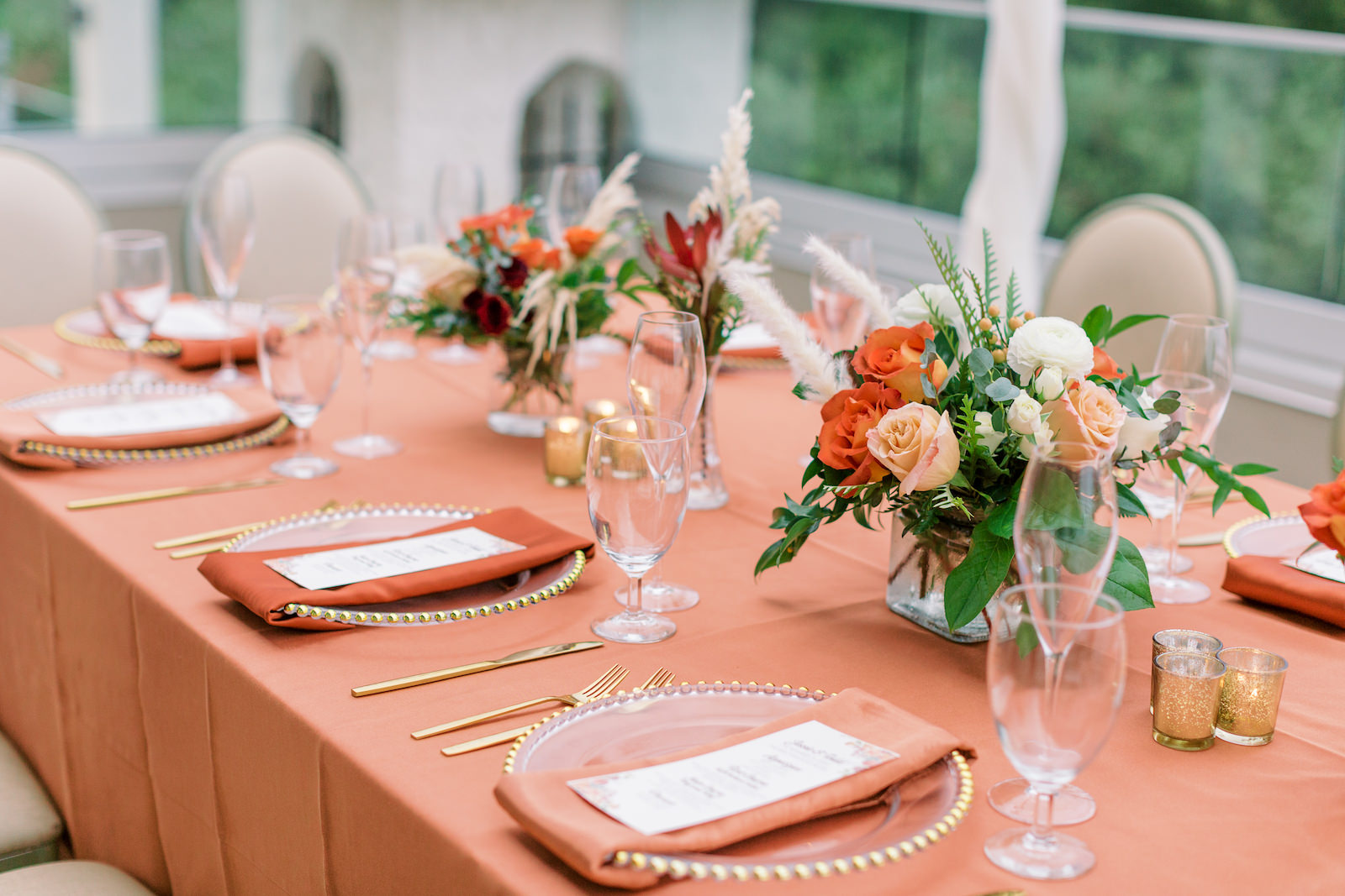 Copper Orange Wedding Reception Table Linens with Gold Beaded Glass Charger Plates topped with Napkin and Menu Card with Gold Flatware | Fall Autumn Wedding Centerpiece with Orange and Peach Roses and Pampas Grass