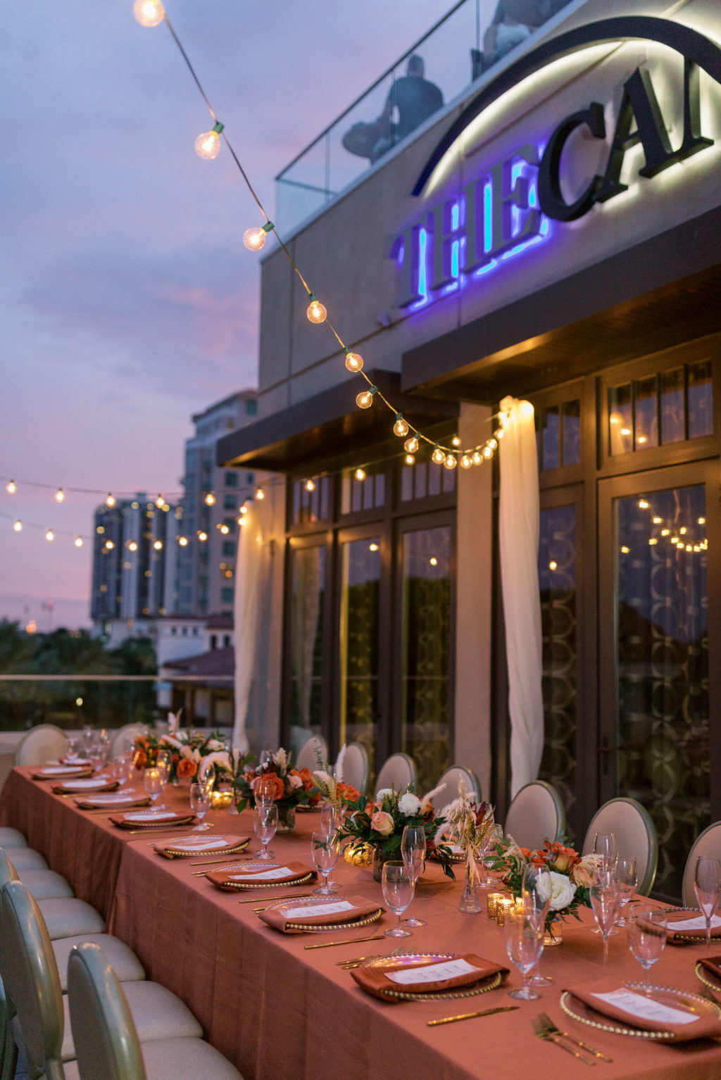 Outdoor Terrace Wedding Feasting Table at St. Pete Wedding Venue The Birchwood | Intimate Micro Wedding Elopement COVID Styled Shoot | Fall Autumn Wedding Inspiration | Hotel Terrace Reception with Canopy String Lights Orange Copper Wedding Table Linens | Gold Beaded Glass Chargers with Napkin and Menu Card and Gold Flatware | Wedding Centerpiece with Orange White and Peach Roses