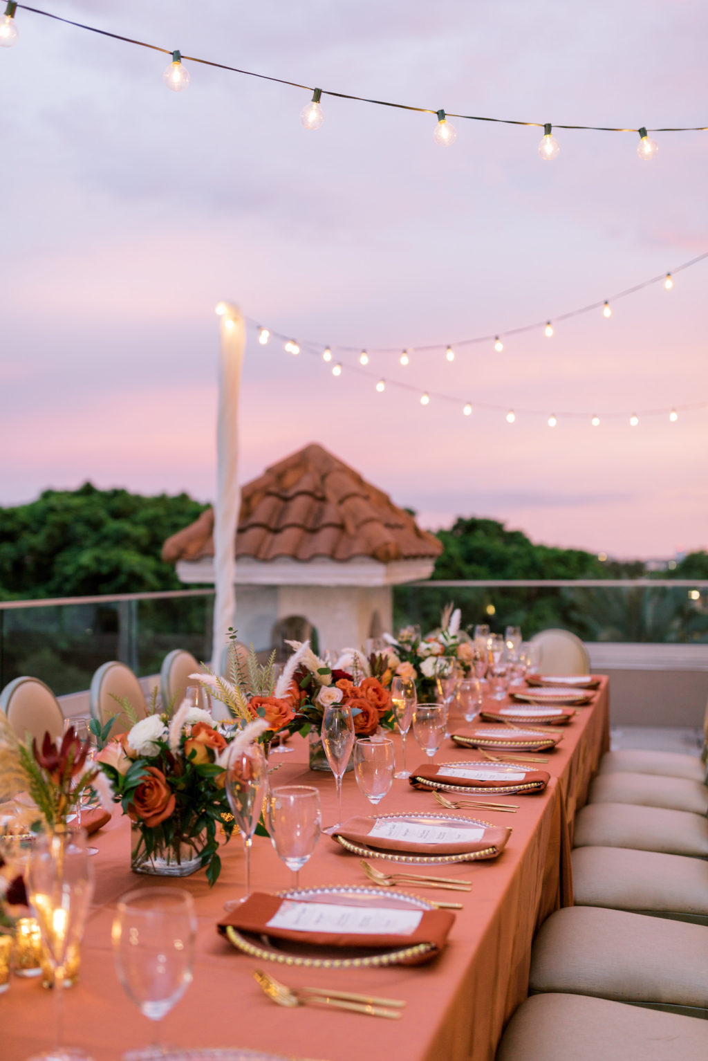 Outdoor Terrace Wedding Feasting Table at St. Pete Wedding Venue The Birchwood | Intimate Micro Wedding Elopement COVID Styled Shoot | Fall Autumn Wedding Inspiration | Hotel Terrace Reception with Canopy String Lights Orange Copper Wedding Table Linens | Gold Beaded Glass Chargers with Napkin and Menu Card and Gold Flatware | Wedding Centerpiece with Orange White and Peach Roses