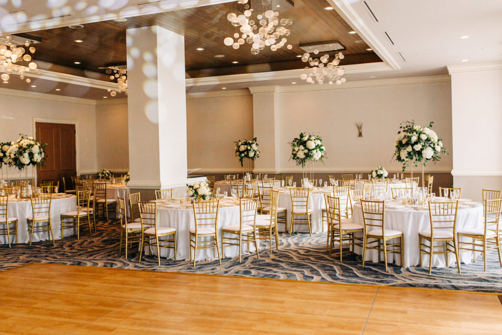 Modern Romantic Florida Wedding Reception and Decor, Round Tables with Gold Chiavari Chairs, Tall Floral Centerpieces with Ivory Roses, White Hydrangeas and Greenery, Clear Chargers with Gold Accent on Rim | Tampa Bay Wedding Florist Bruce Wayne Florals | Clearwater Beach Wedding Planner Special Moments Event Planning | Florida Wedding Venue and Resort Hyatt Regency Clearwater Beach, Bellaire Ballroom