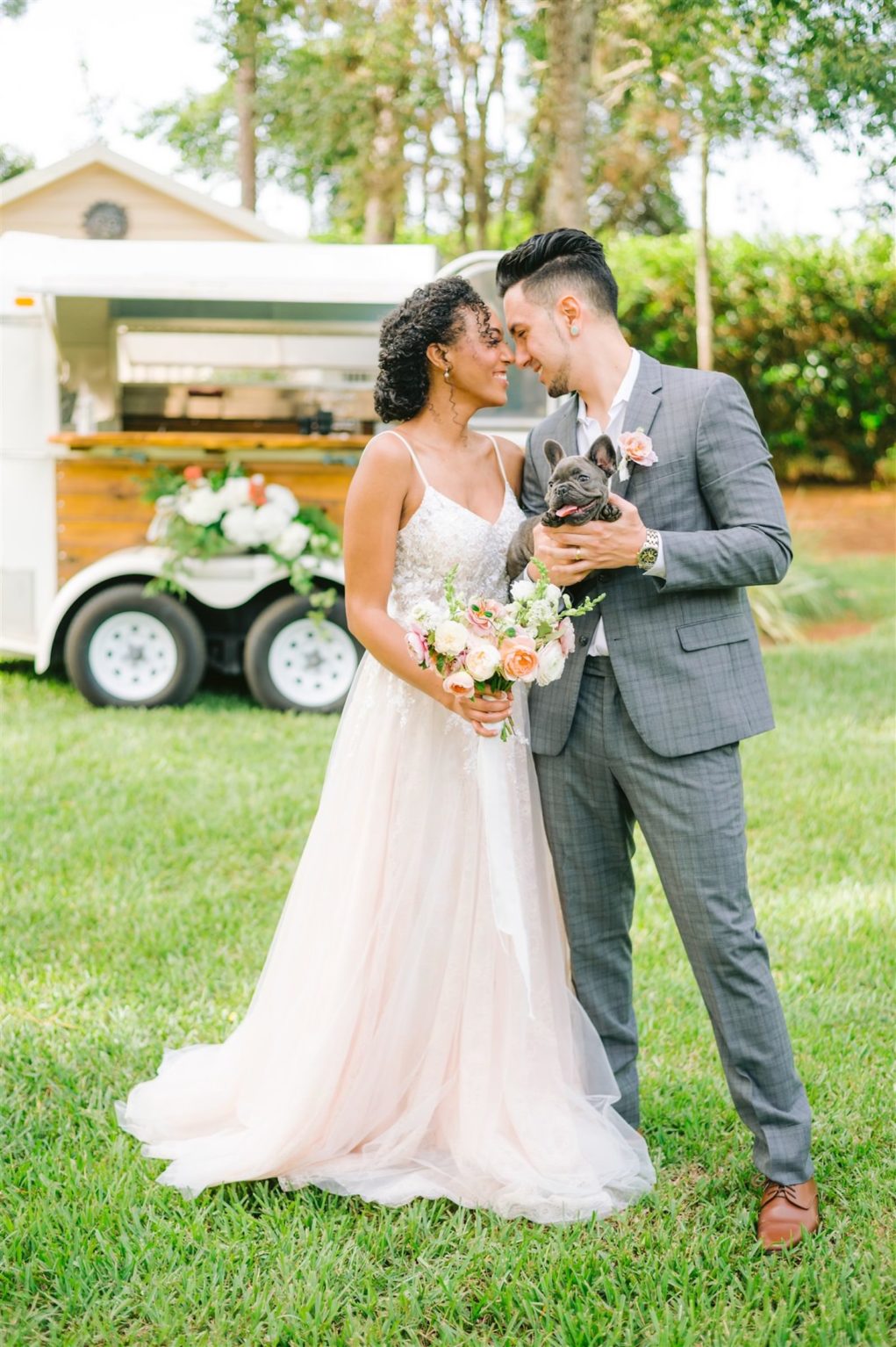 Tampa Bay Bride and Groom Romantic Private Residence Backyard Intimate Wedding, Holding Bridal Bouquet with Triadic Color Scheme, pink, peach and ivory florals, Wearing A Line Spaghetti Strap Wedding Dress with Lace Bodice and Blush Tulle Skirt, Groom in Stylish Gray Plaid Suite, Holding Adoptable Pet Pitbull Puppy | Tampa Wedding Attire Nikki’s Glitz and Glam Bridal Boutique | Tampa Bay Wedding Planner, Designer, Florist John Campbell Weddings | Private Bartending Service Spunky Spirits | Florida Hair and Makeup Artist Michele Renee The Studio | Styled Shoot