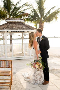Florida Bride and Groom During Intimate Vow Exchange During Beachfront Ceremony under Gazebo, Bride Wearing Made With Love Bridal Tan Sasha Dress, Holding Whimsical Vibrant Inspired Bouquet | Private Tampa Bay Wedding Venue Isla Del Sol Yacht and Country Club | Intimate Wedding Planner Elope Tampa Bay