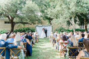 Outdoor Ceremony with Cross Back Wood Chairs at Tampa Wedding Venue Tampa Garden Club | Pipe and Drape Ceremony Backdrop with Eucalyptus Greenery Garland