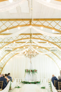 Clearwater Florida Fairy Tale Wedding Ceremony with Gold Arch Ceiling and Draping and Gold Chiavari Chairs | Draped Wedding Ceremony Backdrop with Iron Gate Screen with Greenery Garland and Deep Dark Red Burgundy Roses with Blush Pink Roses and Floating Candles down the Aisle